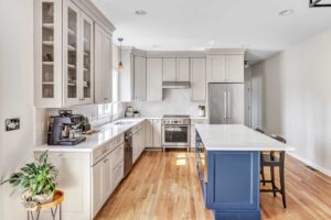 white kitchen cabinets with silver hardware, silver kitchen faucet, white kitchen tile backsplash, blue kitchen island with white countertop