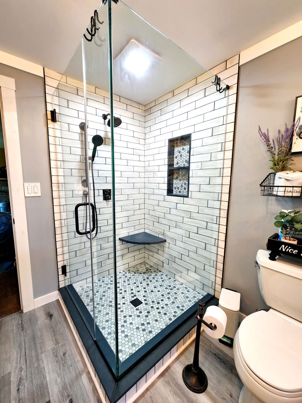 black and white shower with subway wall tiles, wooden floor, white toilet