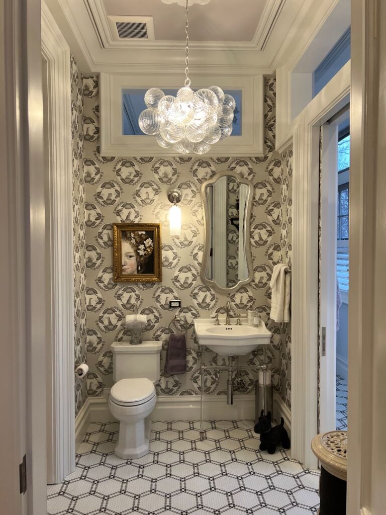 white patterned bathroom tiles, white toilet, white bathroom sink, gray patterned wallpaper, decorative hanging light