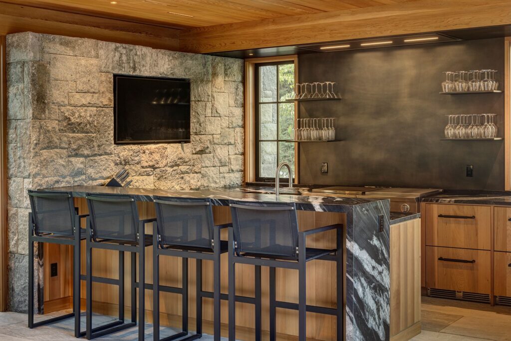 Wood paneled bar, black bar chairs, black marble countertops, win glasses, flatscreen television, stone walls,