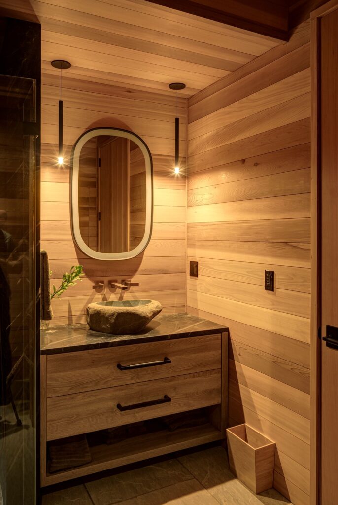 wood paneled bathroom, wooden trash can, wooden paneled cabinets, bright LED light up mirror, stone rock bathroom sink, black drawer handles